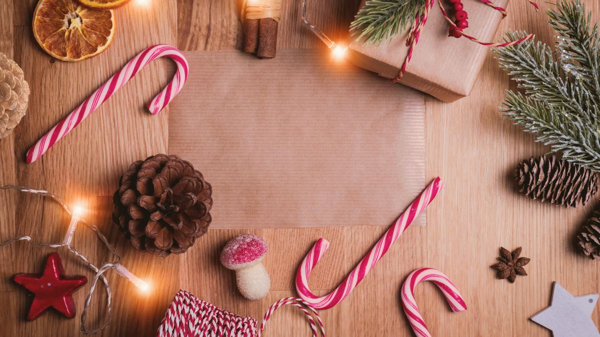 Bild einer Holzplatte auf der Zuckerstangen, Sterne, Zapfen, Geschenken sowie getrockneten Apflesinenscheiben liegen. 