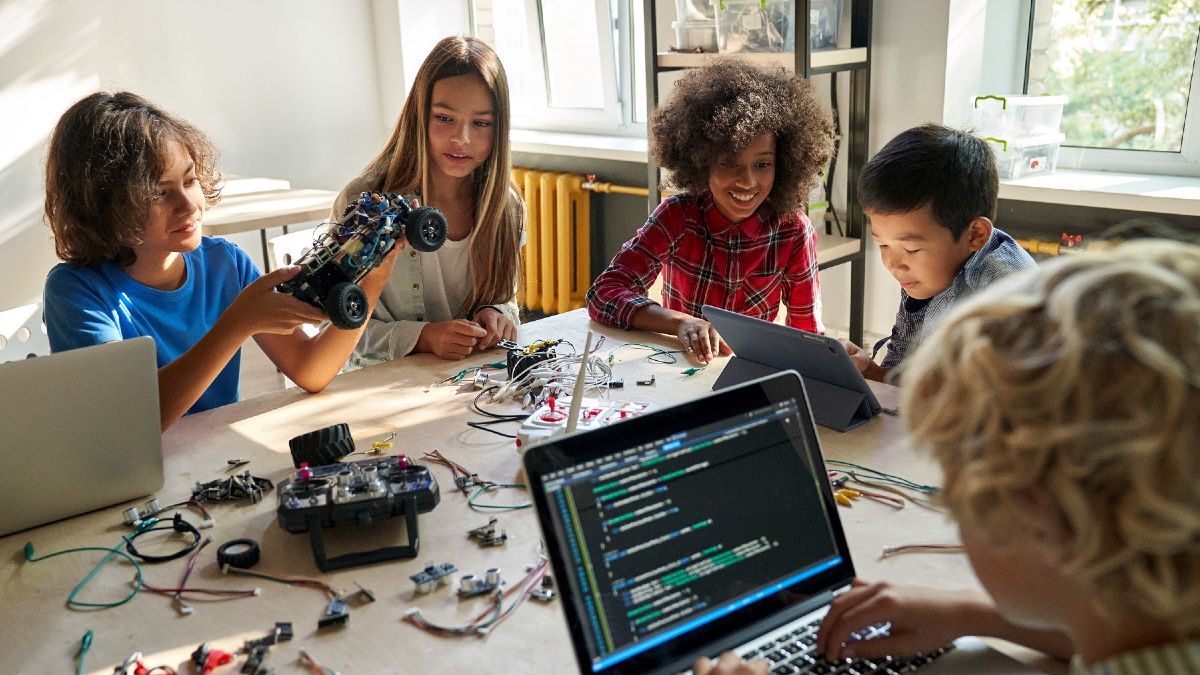 Kinder an einem Tisch voller Laptops und Kabeln/elektronischem Zubehör